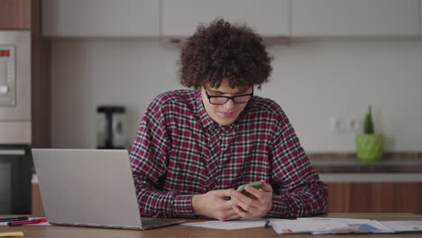 young man with smartphone in his hands. modern businessman or student at home office. freelancer at work. young student man study at home with laptop and uses a smartphone