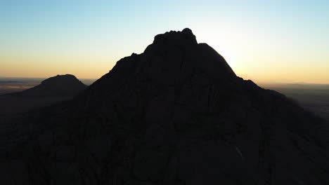 Aerial-view-around-a-silhouette-mountain-in-the-Namib-desert,-sunny-evening-in-Namibia