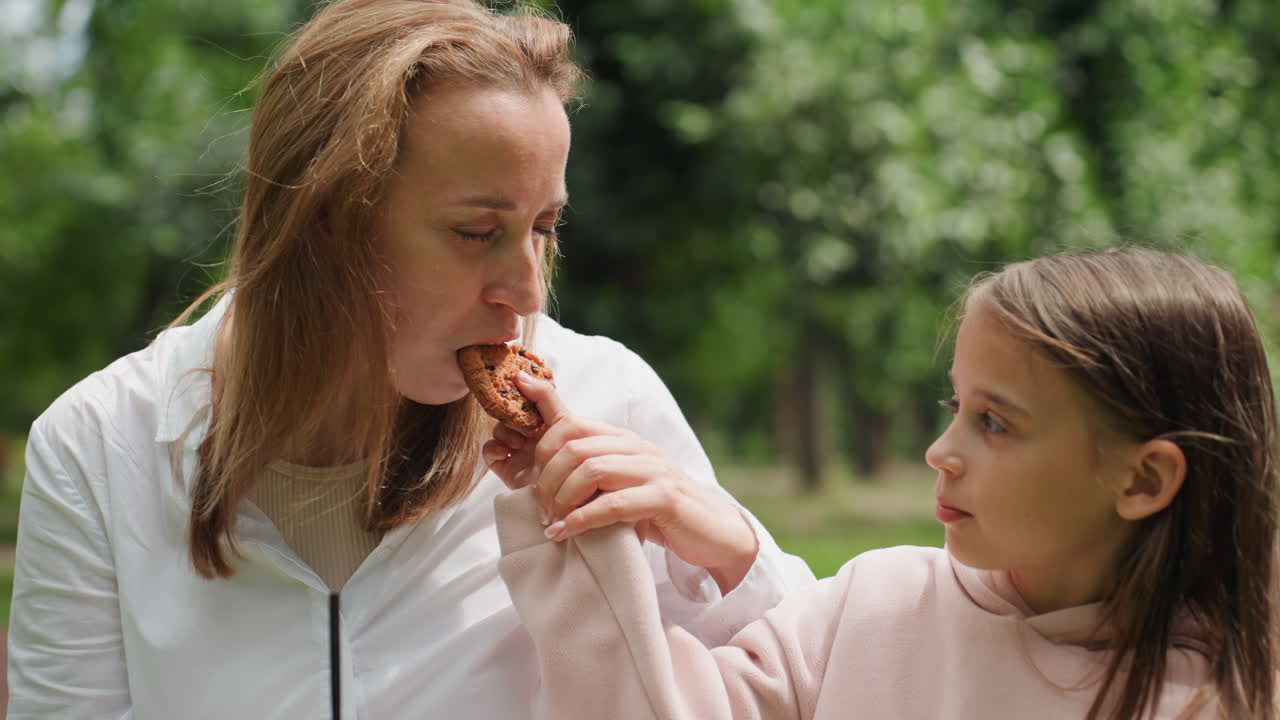 Sharing sweet moment. Mother and daughter exchanging treats peacefully. Loving mother and daughter share pastry in harmony. Mother and child exchange delicacies with gentle smiles in park