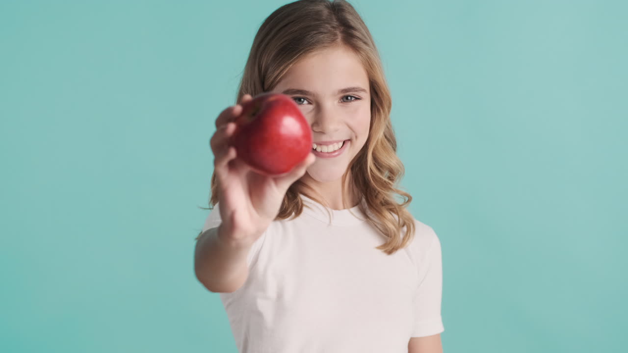 una adolescente caucásica en pijama sosteniendo una manzana y sonriendo.