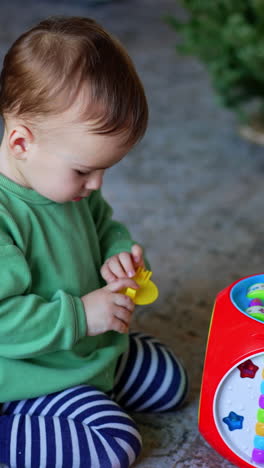 lovely kid looks carefully at the piece that fell apart from his toy. baby boy plays sitting on the floor indoors. vertical video