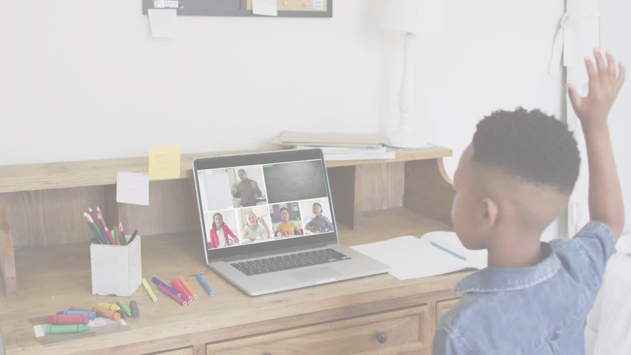 Boy raising hand to answer while teacher calling in online class, laptop overlay growing over desk