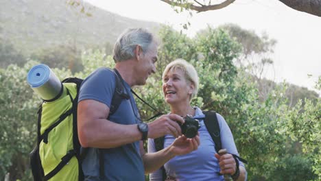 una pareja de excursionistas mayores con bolsas usando una cámara digital en el bosque mientras caminan por las montañas.