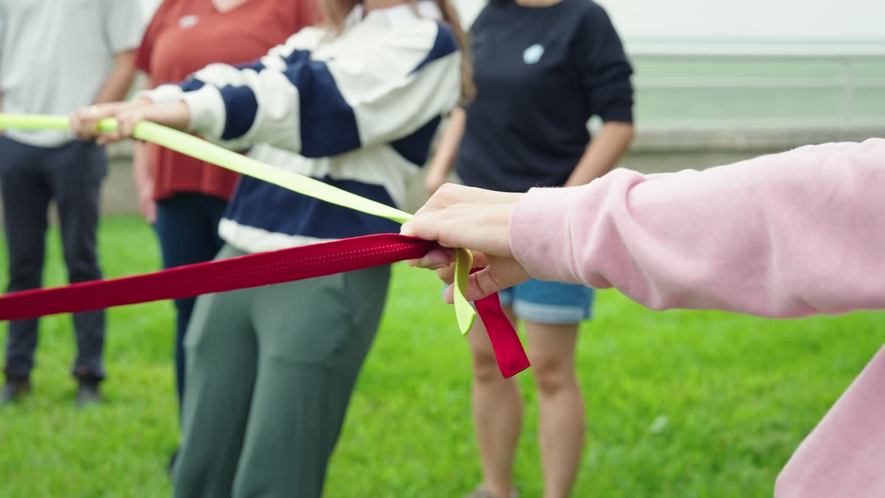 Close up shows woman gripping red strap in circle for outdoor group activity