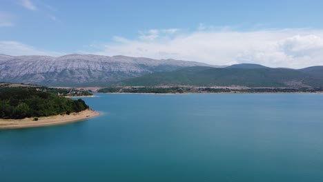 frente al azul profundo del lago croata perucko con una playa brillante, detrás de las imponentes montañas dinara en un clima agradable y soleado