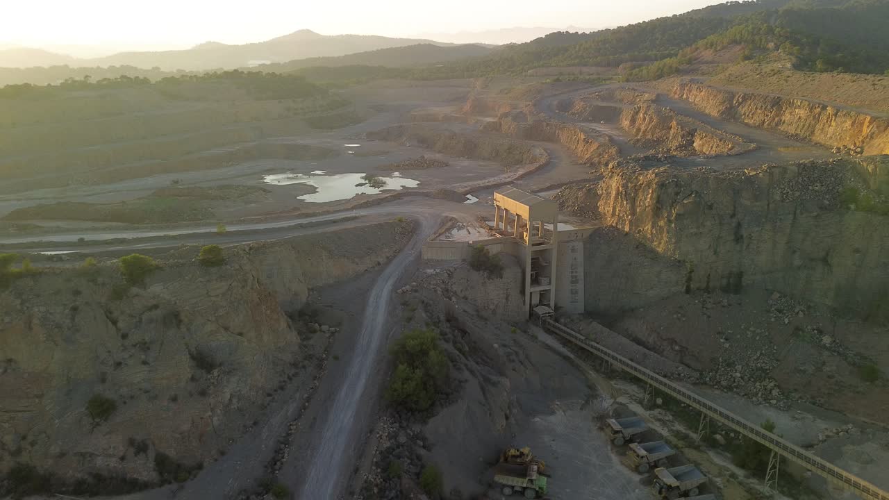 Aerial view of a large open-pit quarry with a processing plant at sunset