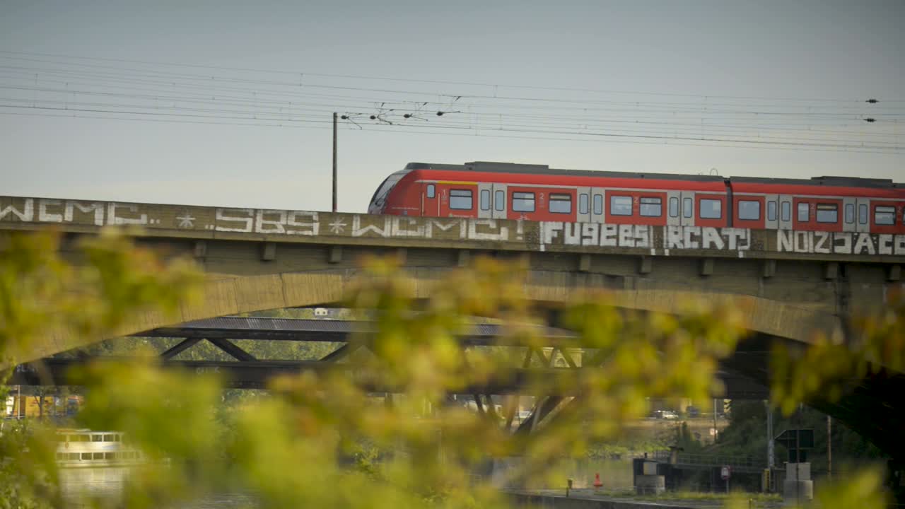 un tren rojo cruza un puente cubierto de graffiti en un día soleado