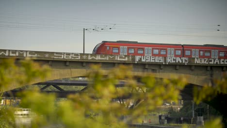 a red train crosses a graffiti-covered bridge on a sunny day