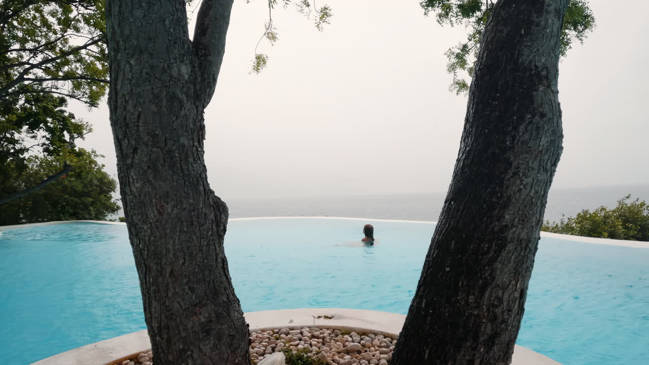 Aufsteigende Kranfahrt von ausgelassenen Frauen in einem Infinity-Pool im Regen.