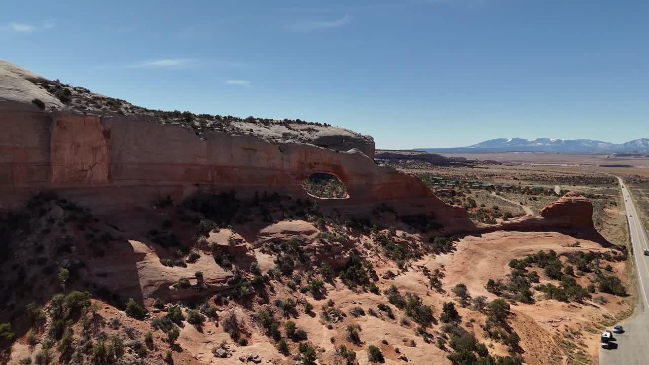 Wilson Arch in Moab Utah, Push in Shot, cars driving on highway, Highway 191, Early Morning, Blue Sky, Mountains in background, Roadside Attraction