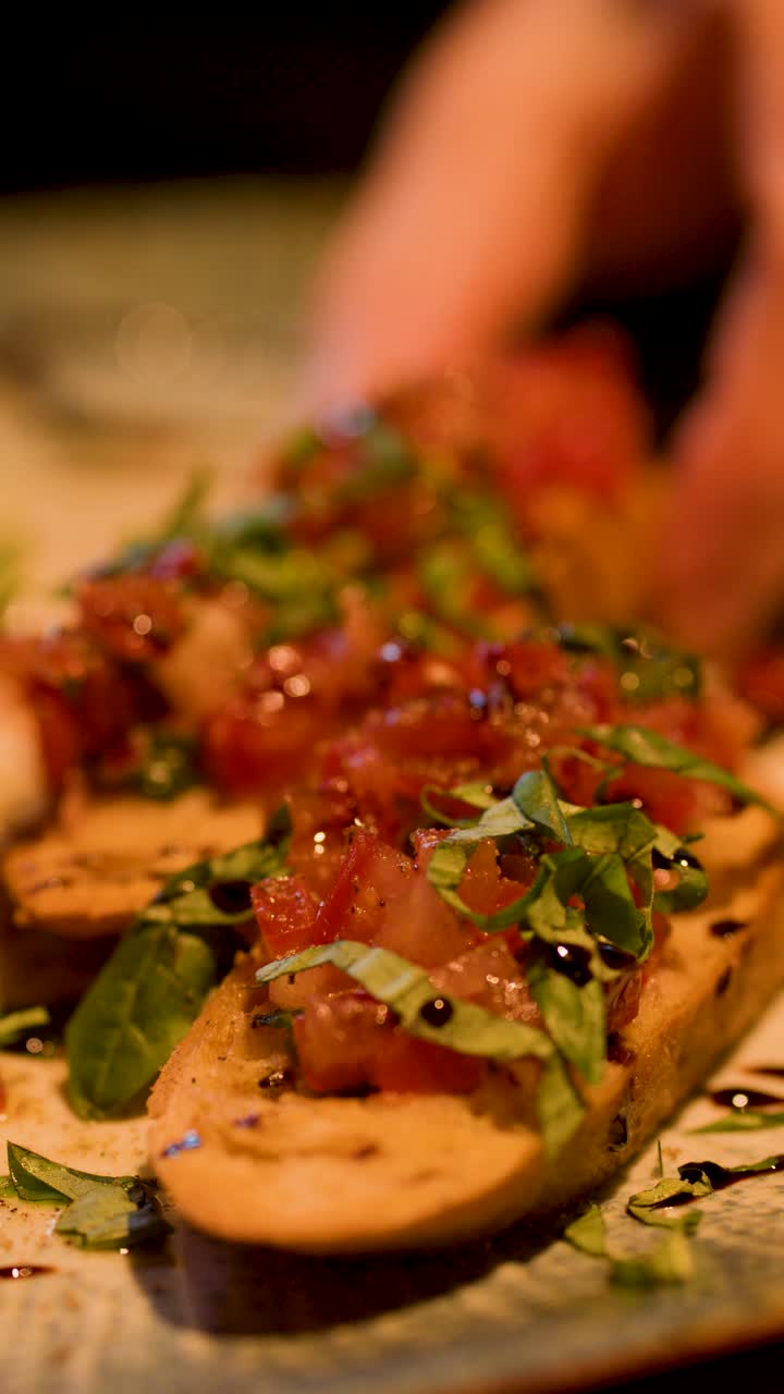 Primo piano di una mano che afferra un antipasto di bruschetta italiana sotto una calda e suggestiva illuminazione da ristorante.