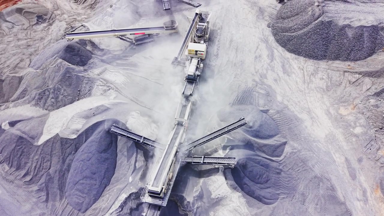 Direct overhead drone shot of mechanical screening unit discharging aggregate onto a symmetric pile. Top down view of gravel sorting conveyor system.