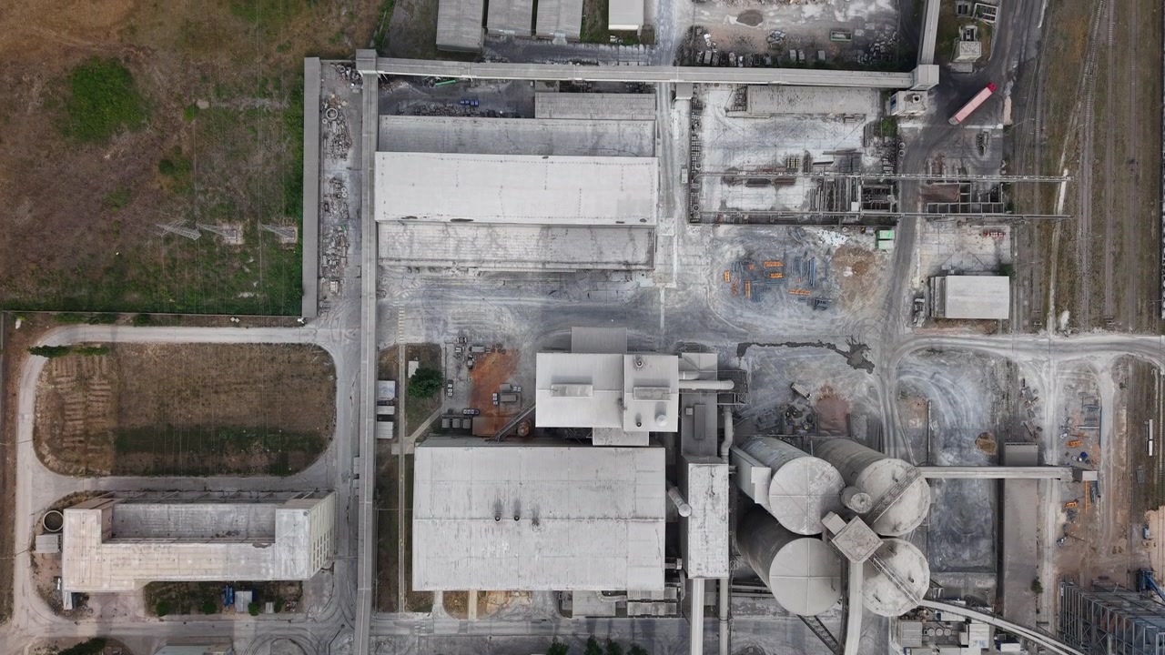 An aerial view captures a sprawling industrial facility with large concrete structures and silos, representing modern manufacturing and economic output.