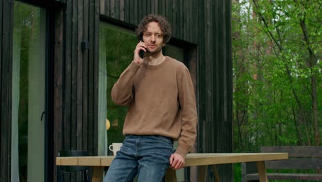 hombre hablando por teléfono fuera de la cabaña de madera