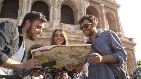 three happy young friends tourists with bikes and backpacks at colosseum in rome reading map guide for directions on sunny day slow motion steadycam ground shot