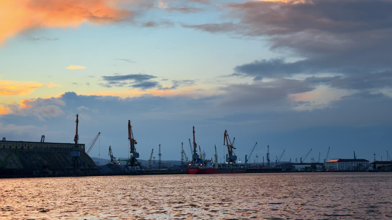 Burgas, Bulgarien, 29 oktober 2025: Solnedgång över hamnen med kranar och fartyg i vattnet. Utsikt över hamnen under solnedgången med fartyg och kranar längs strandlinjen i fjärran.