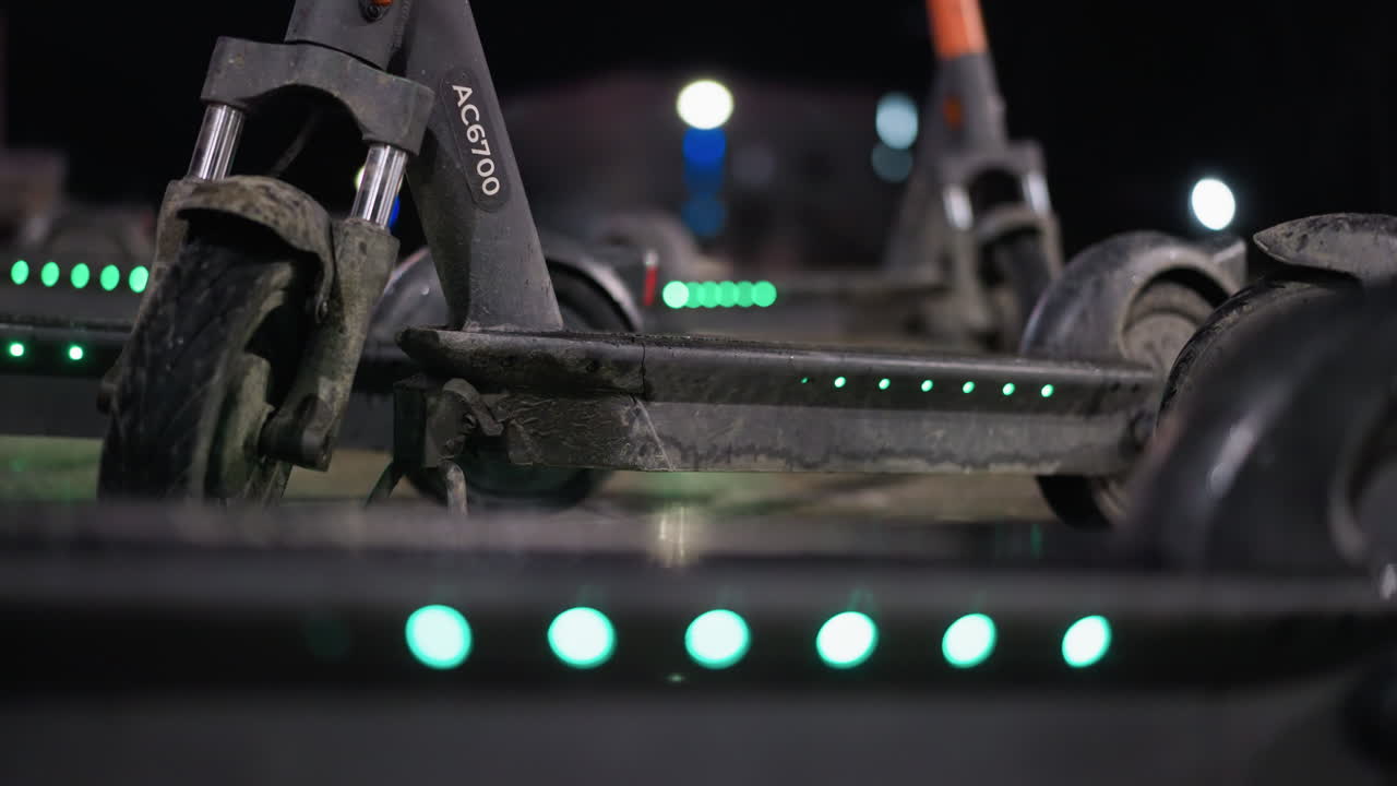 배경에 부드러운 보케 효과와 함께 주차 된 전기 스쿠터 자전거 손잡이의 가까운 시각, 스쿠터의 손잡이에 초점을 맞추고 도시 밤의 흐릿한 불빛