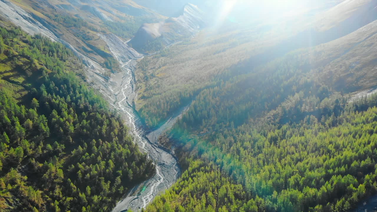 Aerial view of a forested mountain valley with a winding river and sun flare