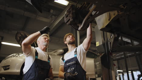 two mechanics inspecting and repairing car suspension