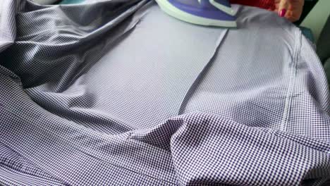 a woman irons a purple shirt with an iron on the table