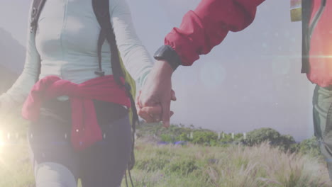 midsection of caucasian senior couple hiking holding hands in countryside over rays of light