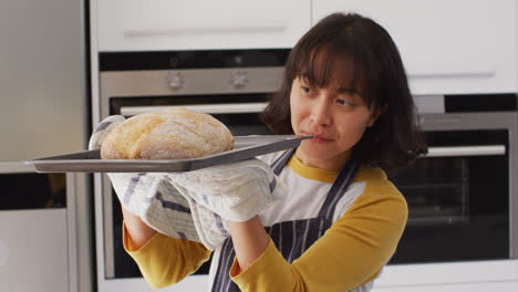 Video-of-happy-asian-woman-taking-out-cake-from-oven