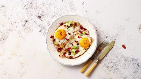 two fresh fried eggs with crunchy crisp bacon and chive served on rustic plate