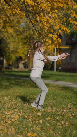 resting woman with disability looks at dancing girl. preschooler with long braids spins scattering dried leaves. mother and daughter on family vacation