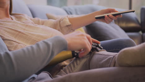 pareja embarazada con mujer con brazo protésico sentada en el sofá en casa juntos viendo televisión