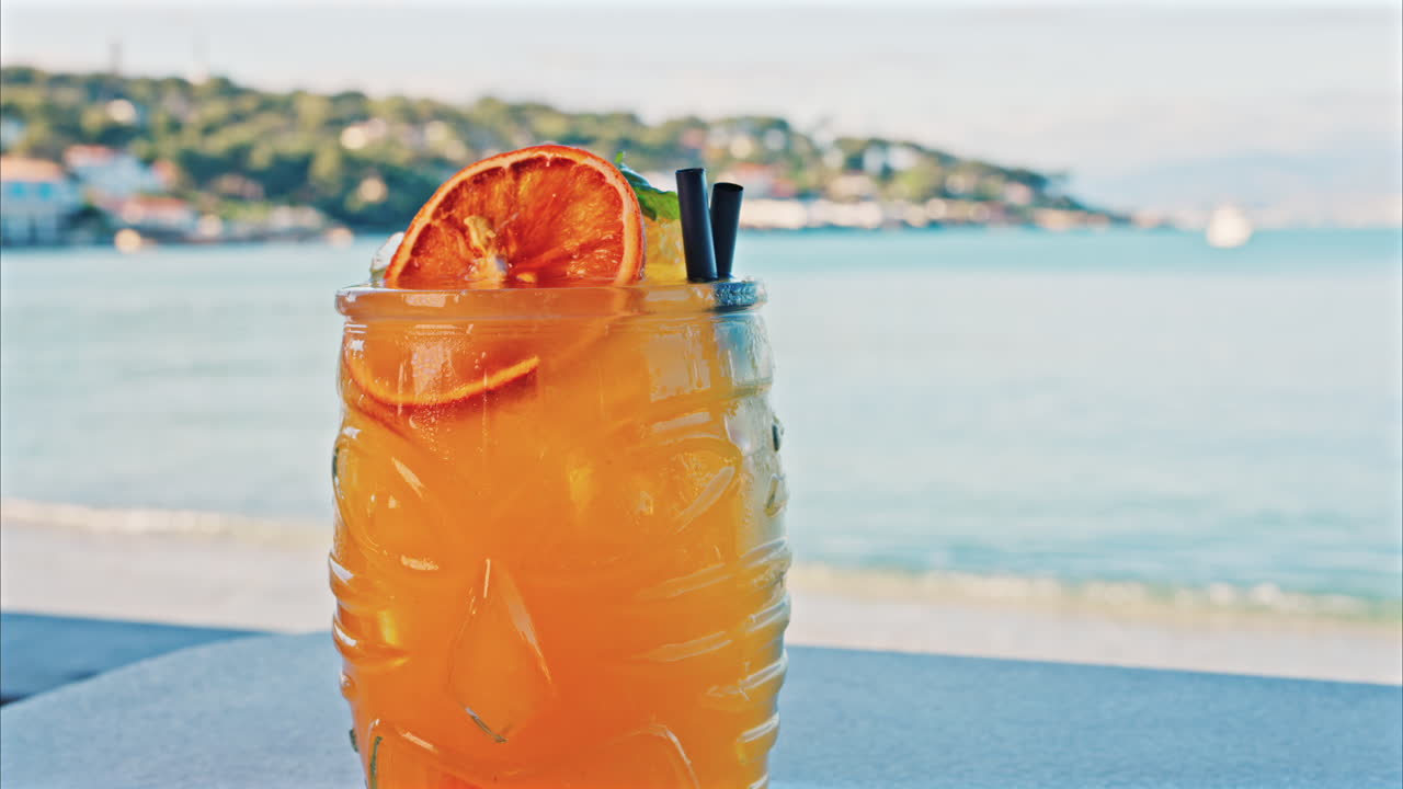 Close up of an orange cocktail on a table with a blurred view of the sea on the background