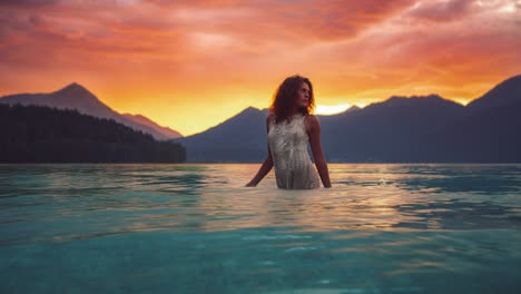 dreamy cinemagraph - seamless video loop of a beautiful young model girl standing in the calm blue and clear water  of lake walchensee in germany-bavaria in a white fashion dress by sunset.