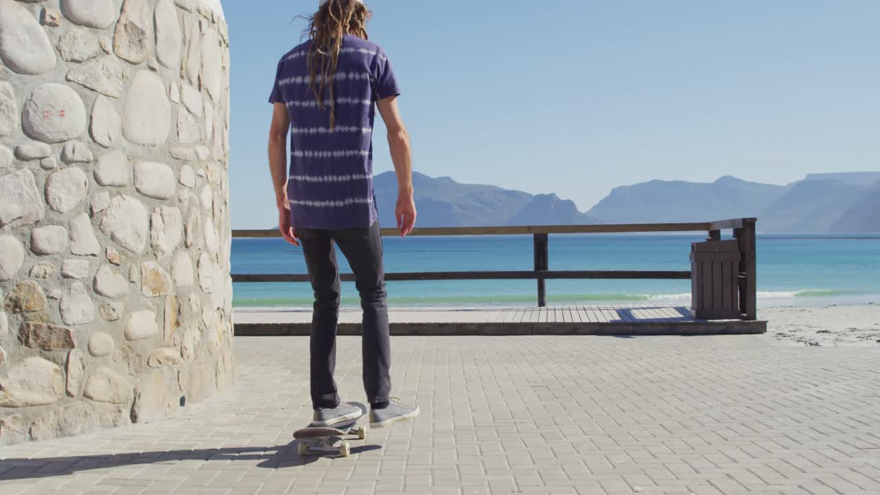 video de un hombre caucásico con dreadlocks patinando en un soleado paseo marítimo