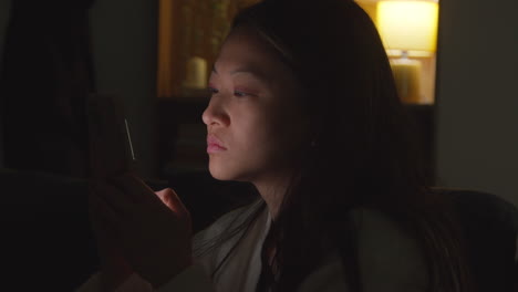 close up of woman spending evening at home sitting on sofa with mobile phone scrolling through internet or social media 5