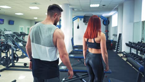 sportive couple come into fitness center. beautiful woman and athlete man in sports wear go to their daily training on the background of modern gym.