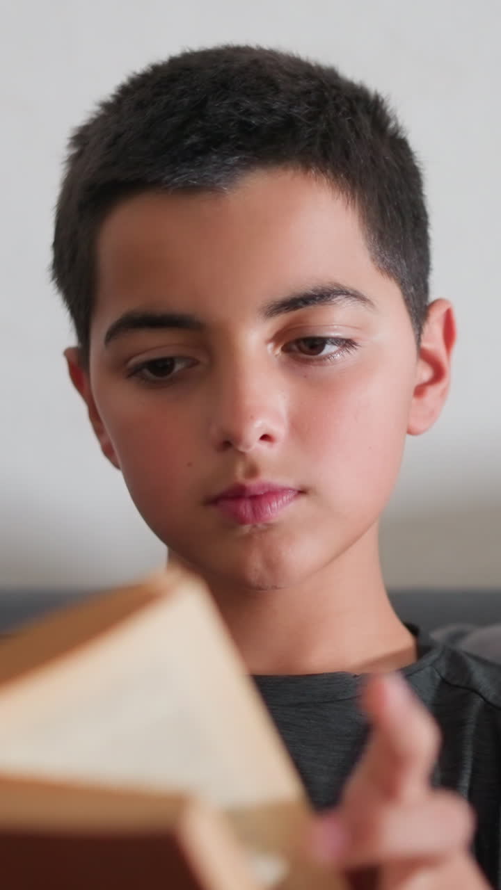 Niño estudiando con gran concentración en el sofá, hojeando las páginas de un libro marrón con expresión de calma, mostrando una gran concentración en el momento de aprendizaje durante una sesión de lectura en interiores