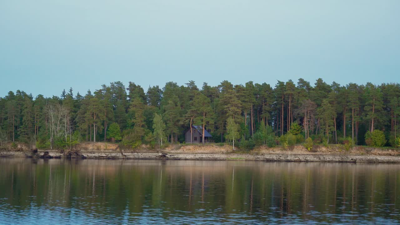 Zoom in shot of a house in the middle of the forest by the river coast.