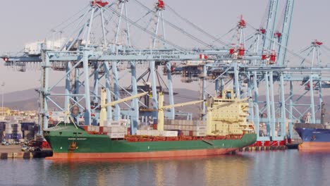 large cargo ship docked at a port with gantry cranes