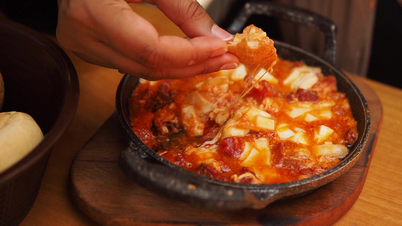 Persona che intinge il pane in un piatto caldo di pomodoro e formaggio