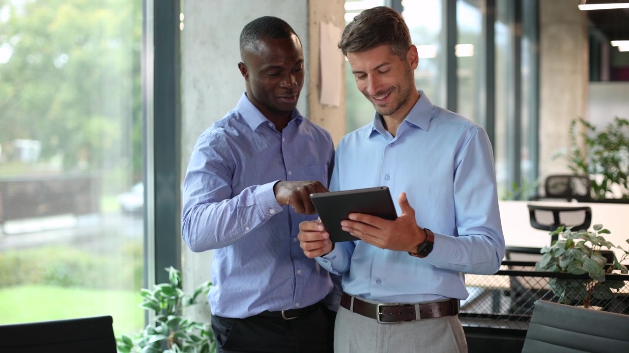Two Diverse Businessmen Discussing Project on Digital Tablet in Modern Office