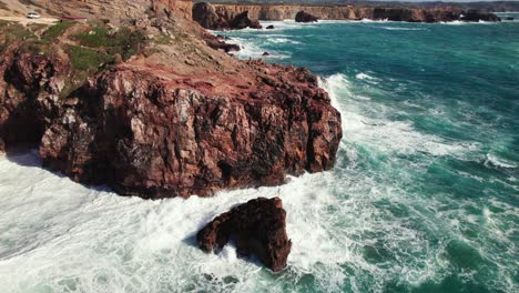 Aerial-4k-drone-circle-view-of-large-crashing-waves-at-Praia-da-Zimbreirinha-hidden-cliff-coastline-near-Bordeira-in-the-Algarve-region-of-Portugal