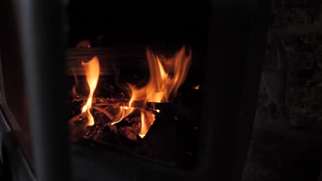 red hot orange fire flame burns sticks and wood in small metal cabin fireplace in slow motion with sparks and embers flying up into flume.