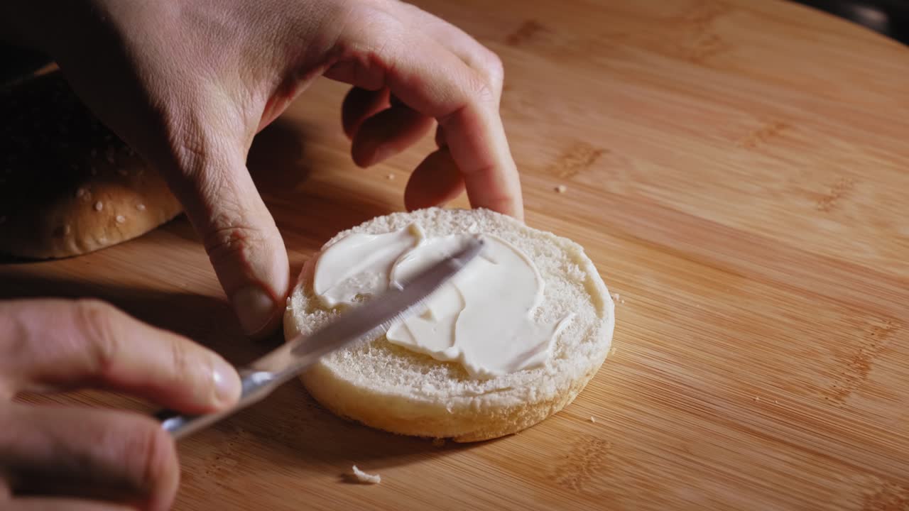 Spreading Mayonnaise On Burger Bun With A Knife, Then Squeezes Ketchup