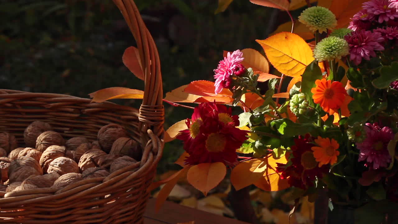 Grande cesto di vimini con noci accanto a un bouquet di fiori su un tavolo all'aperto.