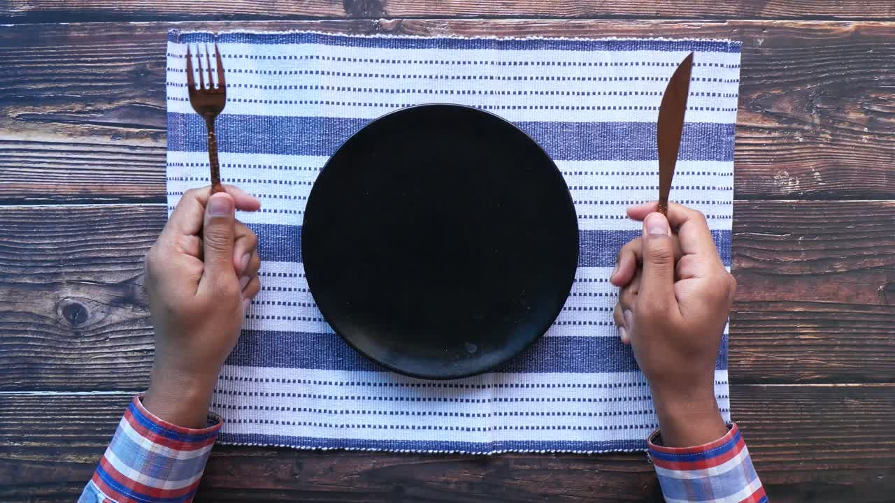persona con las manos sosteniendo un tenedor y un cuchillo en un plato vacío en una mesa