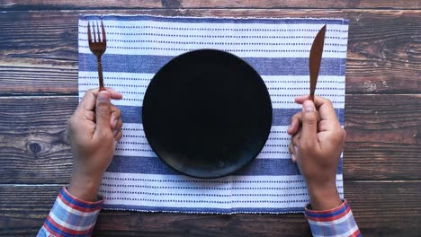 person with hands holding fork and knife at an empty plate on a table