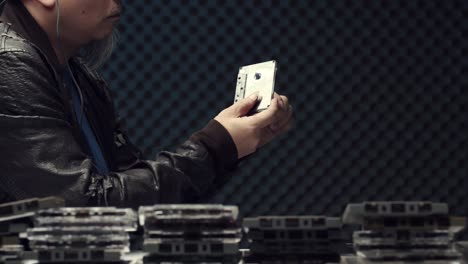 a man in a soundproof room or recording studio rewinds a cassette tape by hand - black egg crate background