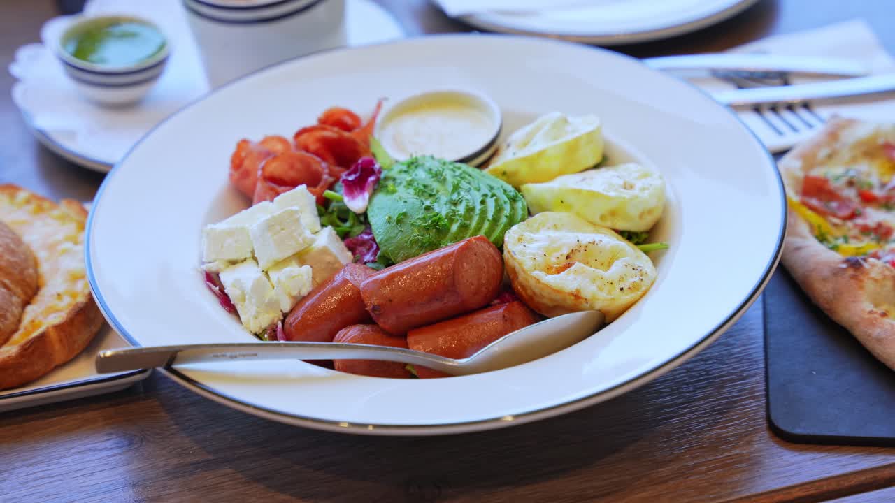 Colorful brunch plate with sausages, feta, eggs, avocado, and salad. Perfect for healthy eating, restaurant, or food styling content