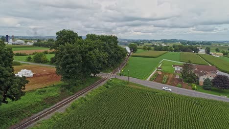 Eine-Luftaufnahme,-Die-Vor-Einem-Antiken-Dampfpersonenzug-Fährt,-Der-An-Einem-Bewölkten-Sommertag-Rauch-Durch-Einen-Bauernhof-Vergnügungspark-Und-Durch-Reiches-Ackerland-Bläst