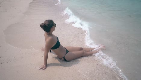 woman-with-hair-bundle-and-in-bikini-sits-on-sand-beach