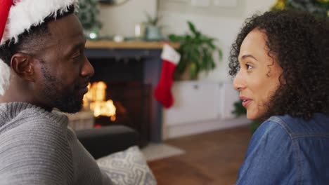 Happy-african-american-couple-sitting-on-sofa-at-fireplace-and-talking
